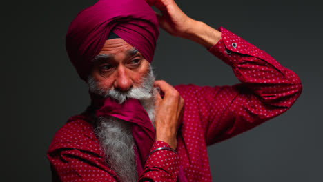 Close-Up-Low-Key-Studio-Lighting-Shot-Of-Senior-Sikh-Man-With-Beard-Using-Salai-Needle-When-Putting-On-Turban-Against-Dark-Background-Shot-In-Real-Time